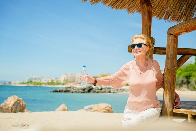 Senior woman sitting on the beach with a bottle of water