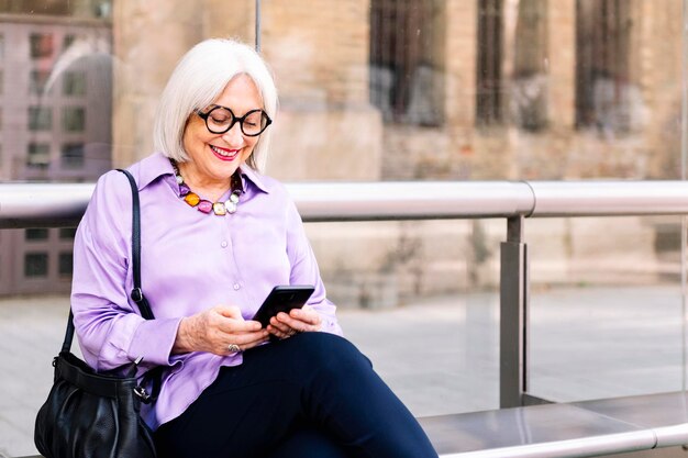 Senior woman sitting at the bus stop using phone