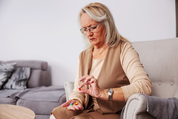 Senior woman sitting at home in her chair and holding hand full of pills and vitamins.