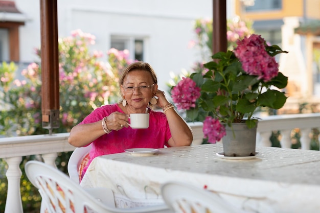 Senior woman sitting on porch enjoing her retirement Wellgroomed elderly woman sitting on the terrace and drinking coffee