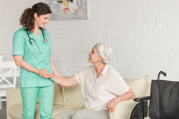 Senior woman sitting on sofa holding nurse's hand