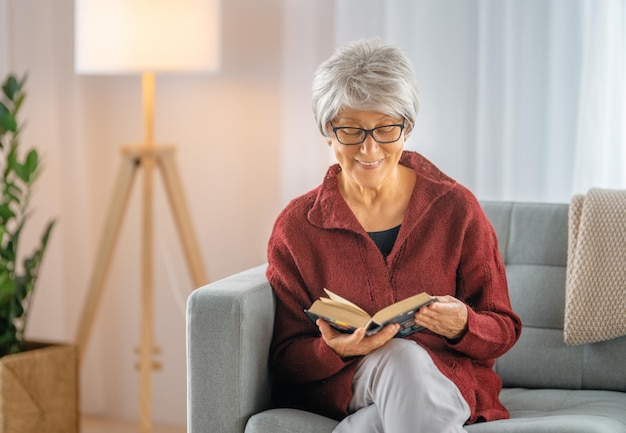 Senior woman sitting on the sofa and reading a book in the room at home.