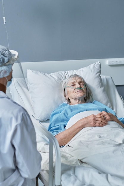 Photo senior woman sleeping in the hospital bed with doctor observing her at the ward