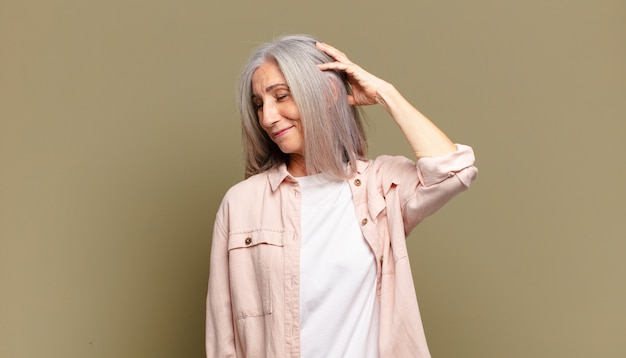 Senior woman smiling cheerfully and casually, taking hand to head with a positive, happy and confident look