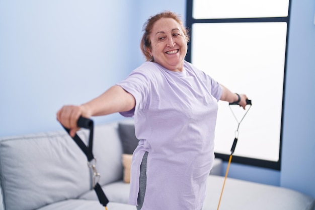 Пожилая женщина уверенно улыбается, используя тренировку с эластичной лентой дома