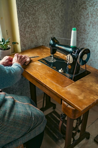 Senior woman in spectacles use sewing machine wrinkled hands of the old seamstresselderly woman Old sewing machine Classic retro style manual sewing machine ready for sewing work