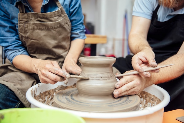 Senior woman spinning clay on a wheel with teacher at pottery class