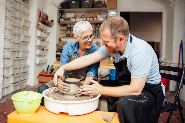 Senior woman spinning clay on a wheel with teacher at pottery class