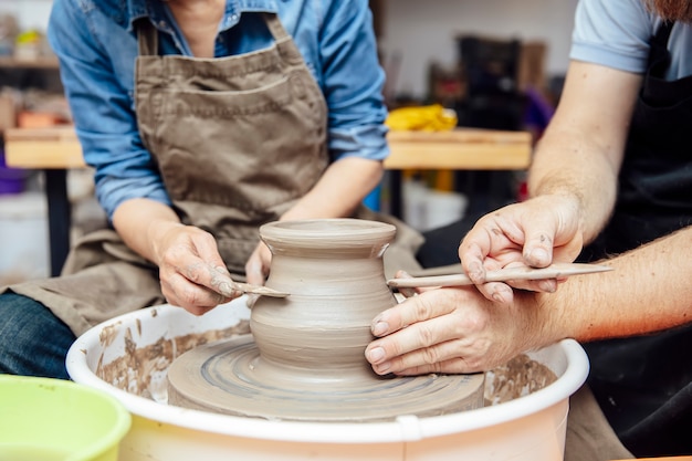 Senior woman spinning clay on a wheel with teacher at pottery class