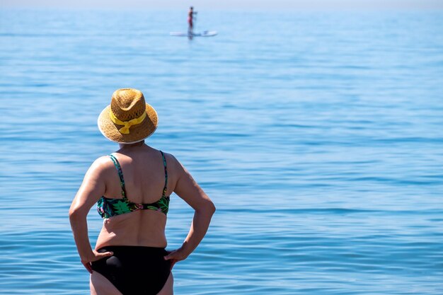 Senior woman standing alone in front of the mediterranean sea at a beach in a sunny summer day