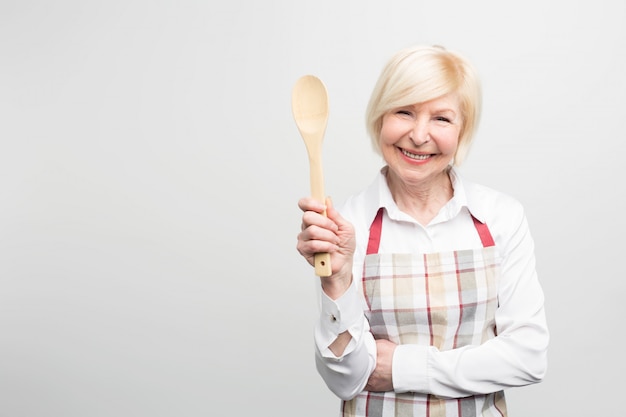 Senior woman standing and holding a spoon. She is a good housewife. She likes to cook tasty food.