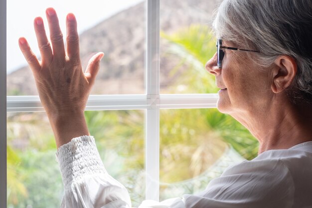 Senior woman stay home at the window looking out