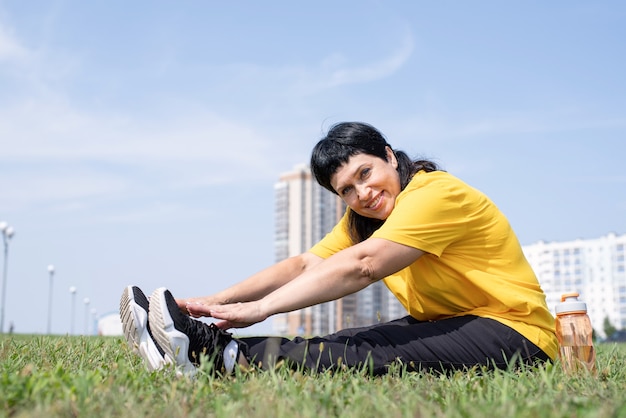 Senior woman stretching her legs on grass in the park