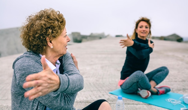 Senior donna che si estende con allenatore femminile dal molo del mare