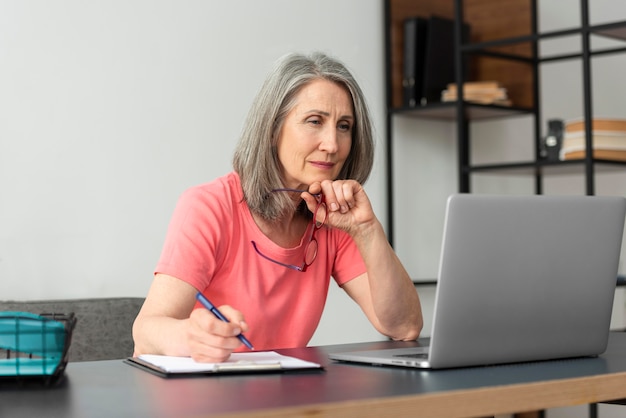 Foto donna anziana che studia a casa mentre usa il laptop e prende appunti