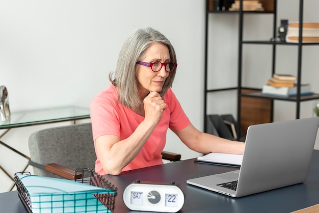 Donna anziana che studia a casa mentre usa il laptop