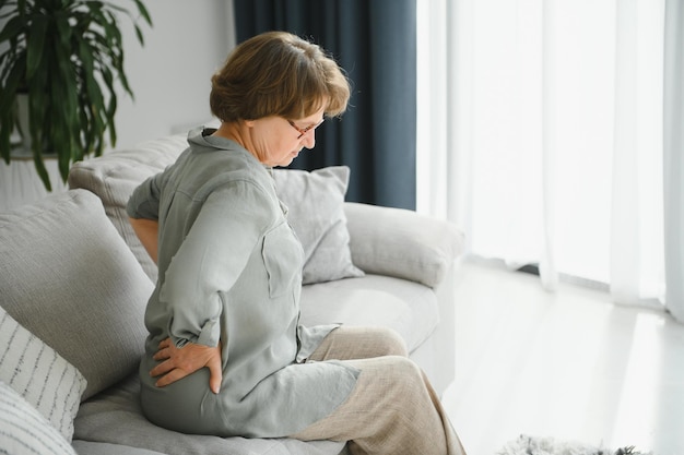 Senior woman suffering from back pain on sofa at home