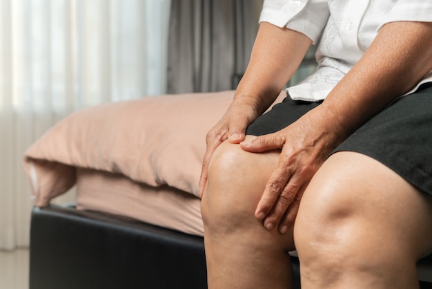 Senior woman suffering from knee pain at home, health problem concept