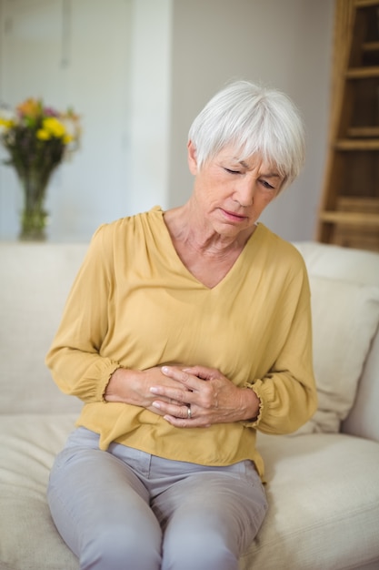Senior woman suffering from stomach pain in living room