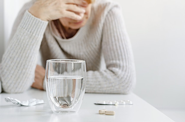 Senior woman suffering and taking pills from migraine. Headache treatment concept.