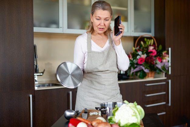 Senior woman talking on phone in kitchen and preparing food