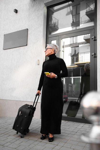 Senior woman tourist with luggage near hotel