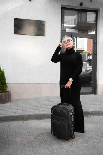 Senior woman tourist with luggage near hotel