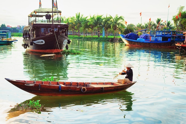 Senior woman in traditional vietnamese hat on a boat in Thu Bon River in Hoi An, Vietnam