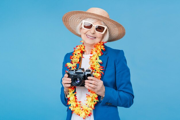 青い背景に分離されたレトロな写真カメラを持つ年配の女性旅行者