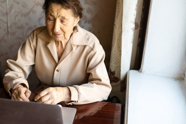 Senior woman use laptop. She looks very surprised. Surfing in a browser and social media. Laptop on the table. Using technology in old age concept