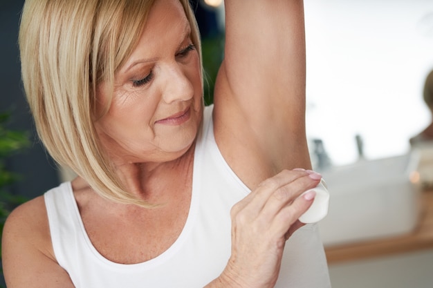 senior woman using deo roll-on in the bathroom