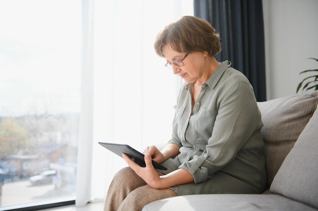 Senior woman using digital tablet in living room at home