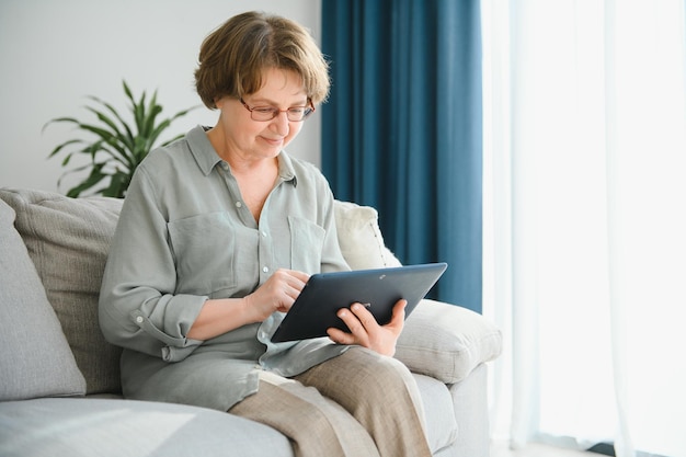 Senior woman using digital tablet in living room at home