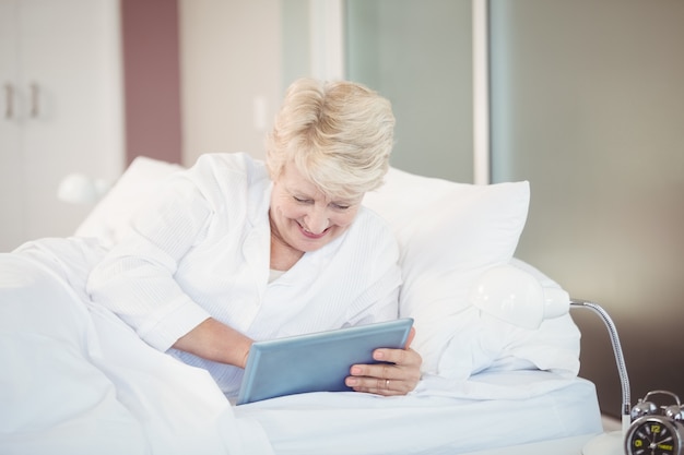 침대에서 쉬고있는 동안 디지털 태블릿을 사용하여 고위 여자