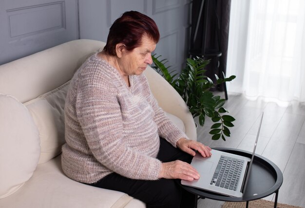 Фото Пожилая женщина использует ноутбук на столе дома