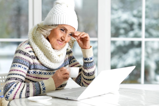 Photo senior woman using laptop, sitting near window