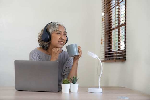 Senior woman using laptop while wearing headphones at home Joyful elderly lifestyle and technology concept