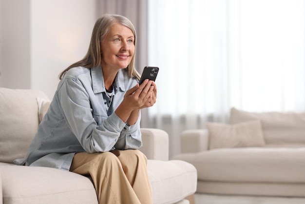 Senior woman using mobile phone at home space for text