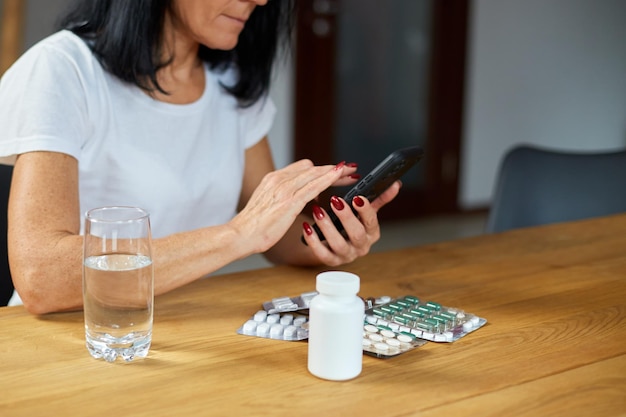 Senior woman using mobile phone ordering medicine pills online at home