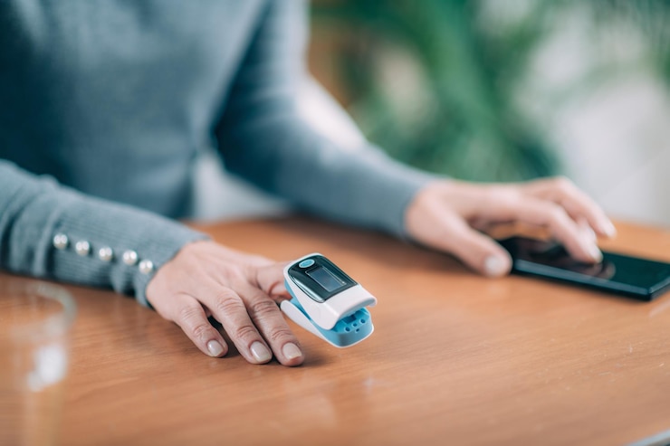 Photo senior woman using pulse oximeter and smart phone measuring oxygen saturation