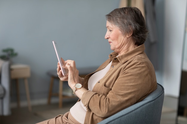 Foto senior donna utilizzando un tablet seduto su una sedia in soggiorno