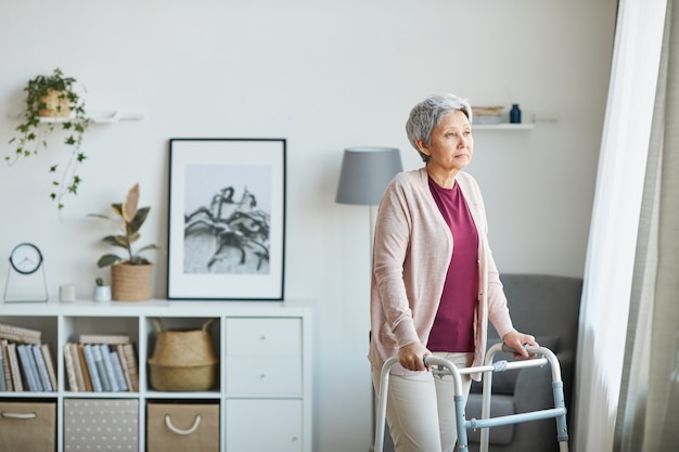 Senior woman walking around the room with the help of walker she is at home