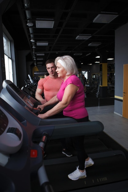 Senior woman walking on a treadmil exercising with fitness coach