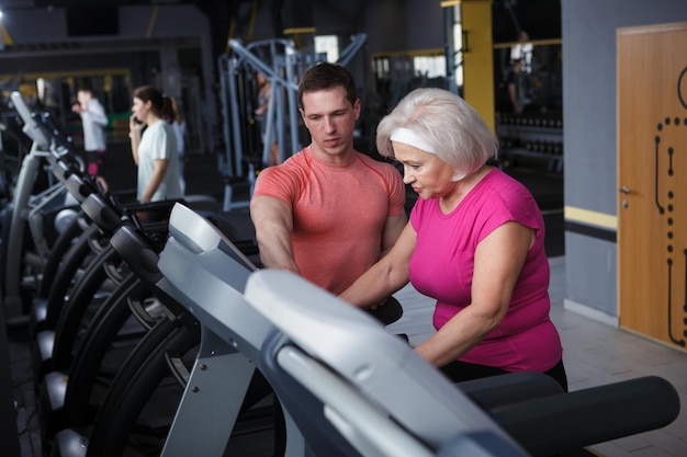 Senior woman walking on treadmill under personal trainer supervision