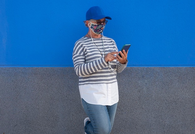 Senior woman wearing flu mask using phone against wall