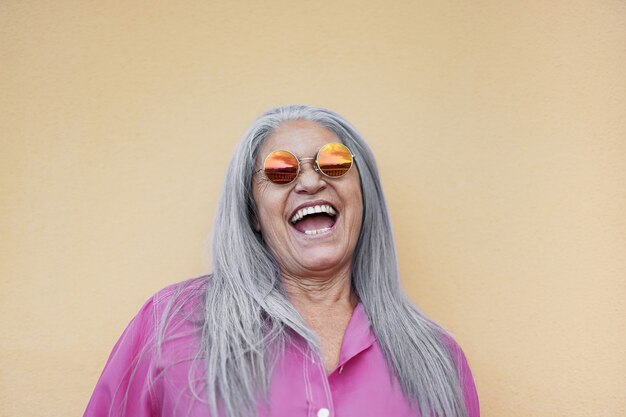 Senior woman wearing hippie sunglasses while laughing on camera - Gray hair granny smiling