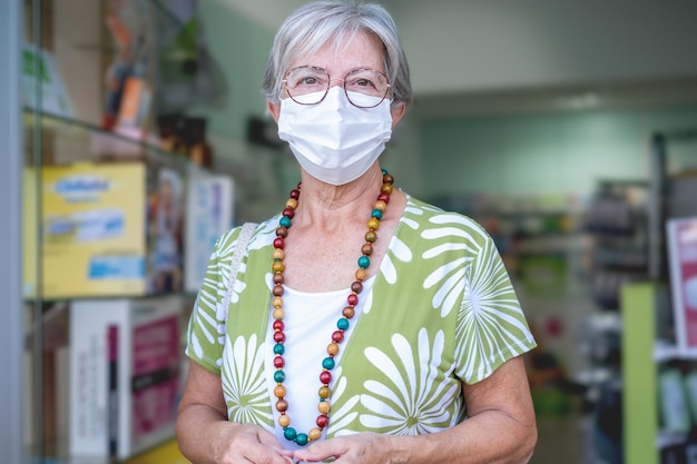Senior woman wearing mask entering in pharmacy to buy medical products Portrait of handsome elderly lady in drugstore pharmacy