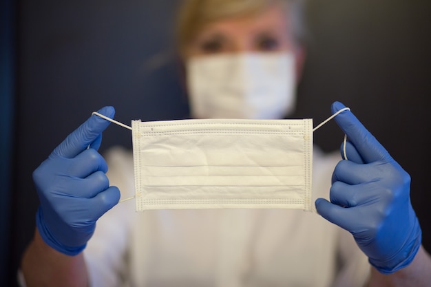 Senior woman wearing mask, gloves holds a a mask in hands. Selective focus. Coronavirus