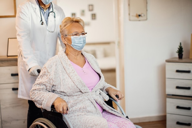 Senior woman in wheelchair getting help from unrecognizable caregiver at nursing home during COVID19 pandemic