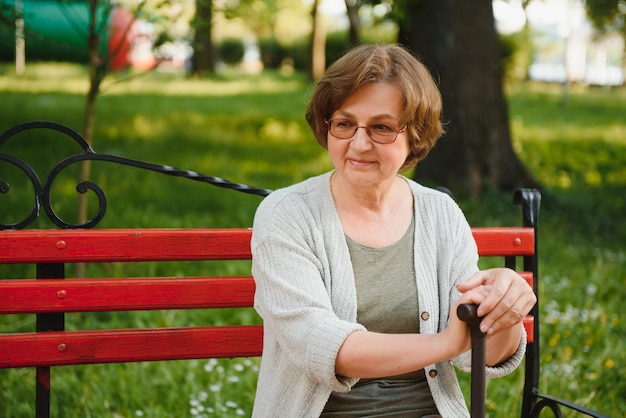 Фото Пожилая женщина с тростью сидит на скамейке в парке